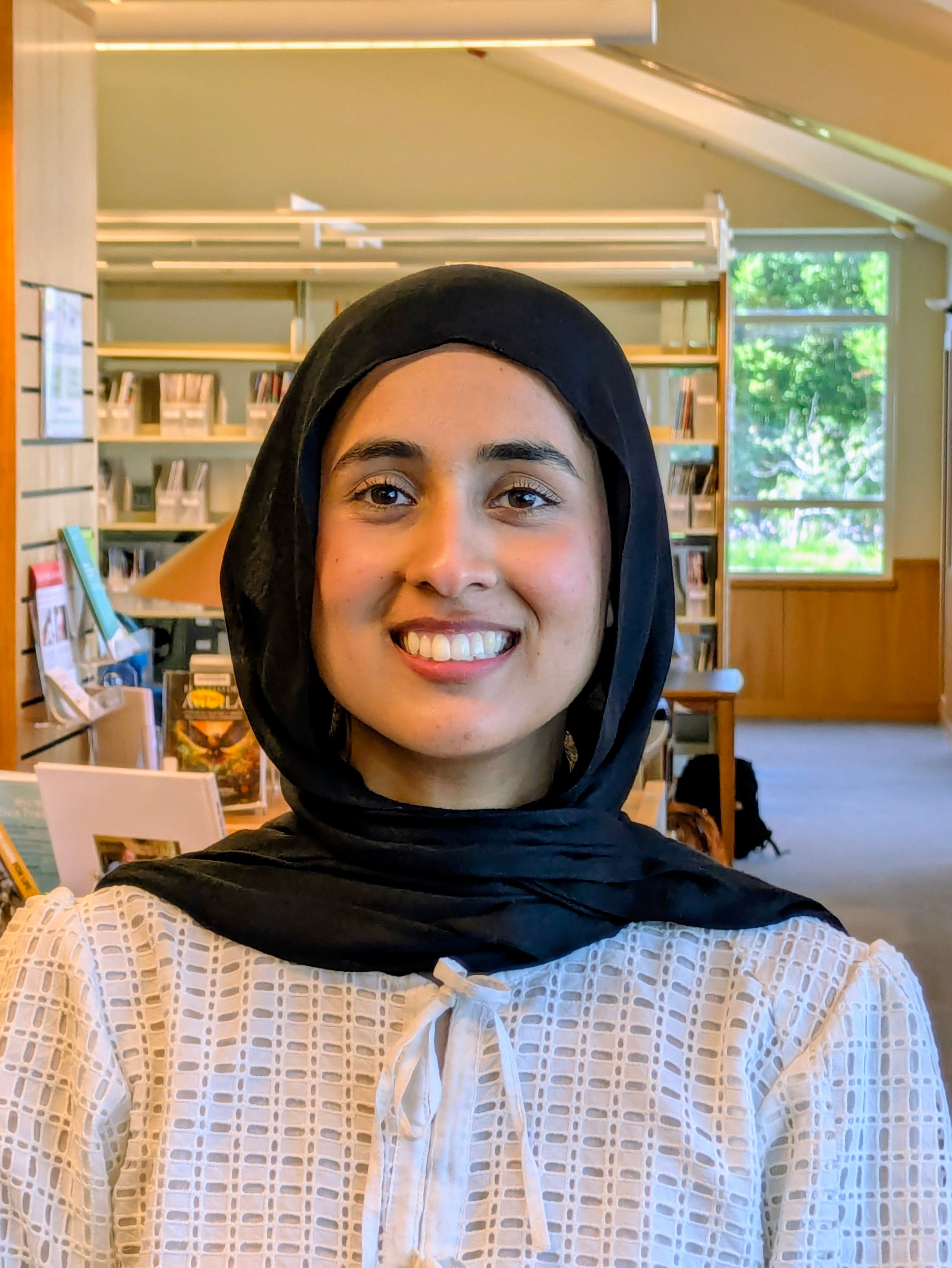 A smiling young woman in a hijab standing in a library