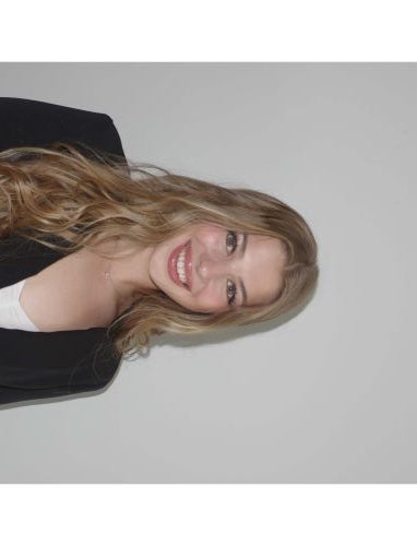 A young woman in a suit jacket smiles at the camera against a white background