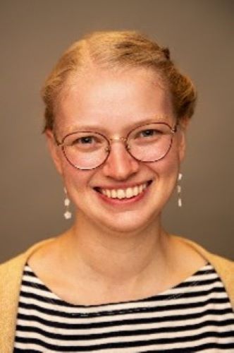 A young woman smiles at the camera against a tan background