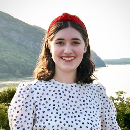 A young lady smiles at the camera while standing in front of a mountain lake