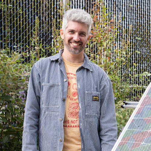 A young man in a garden smiles at the camera