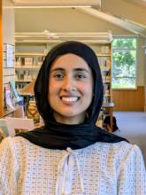 A smiling young woman in a hijab standing in a library