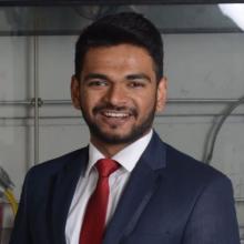 A young man in a suit smiles at the camera
