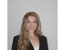 A young woman in a suit jacket smiles at the camera against a white background