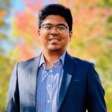 A young man in a suit smiles at the camera